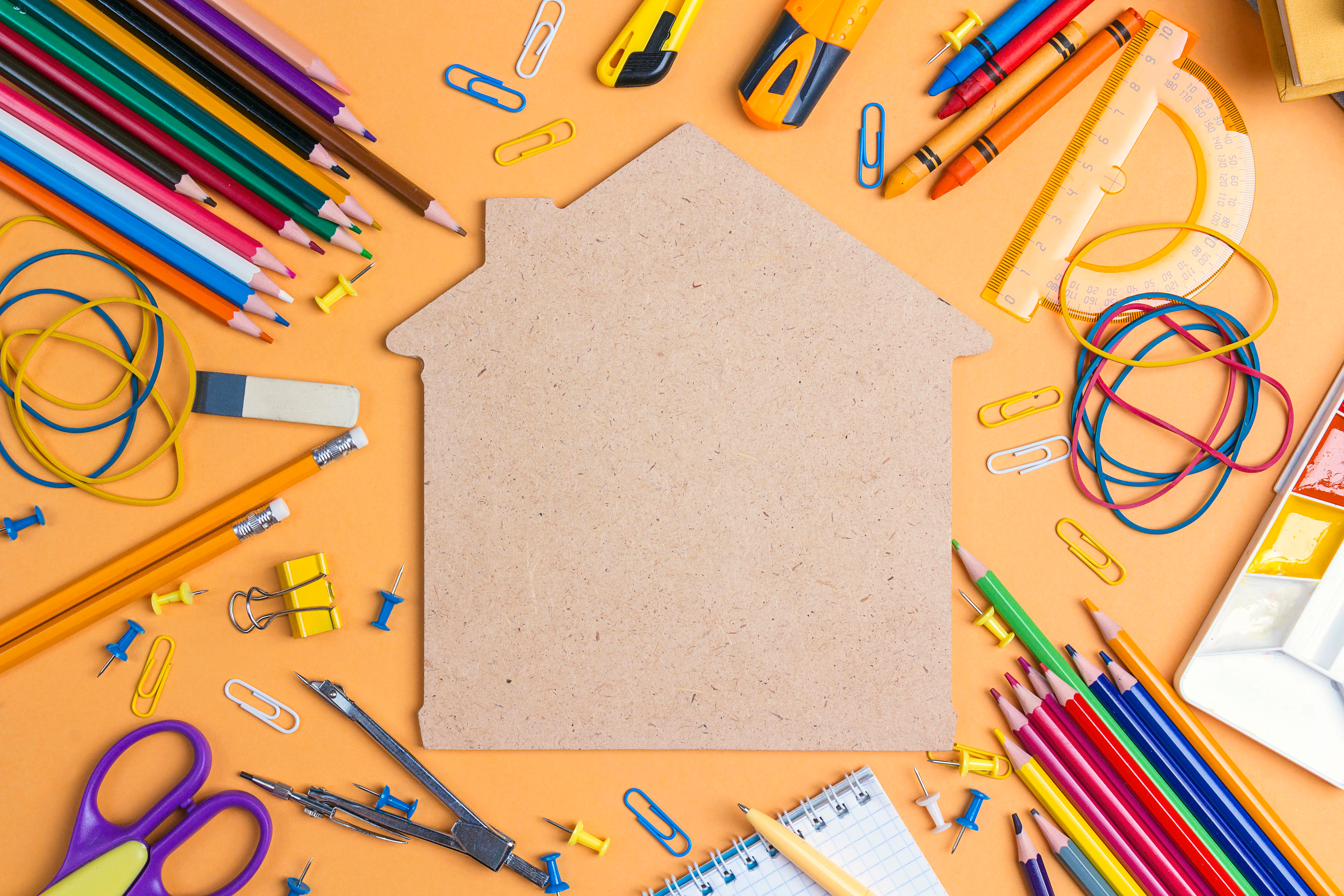 color pencils, crayons, rubber bands and scissors around a house shape